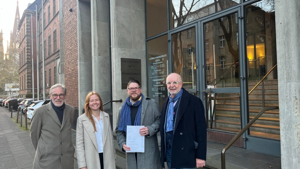 Bild v.L.R.: Dr. Jürgen Küttner, Dr. Alena Diepold (teipel.law), Friedrich Jeschke (Volt), Walter Leo Schreinemacher (Freie Wähler) stehen vor dem Verwaltungsgericht in Köln. Sie stehen vor dem Gebäude.